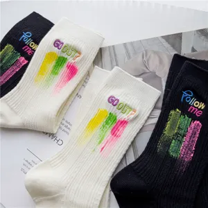 Chaussettes mi-tubes côtelées noires et blanches avec lettres brodées et art au pinceau.