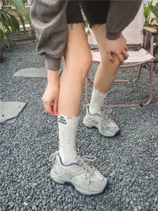 Primo piano di calzini bianchi strappati alla moda con lettere nere e sneakers spesse.