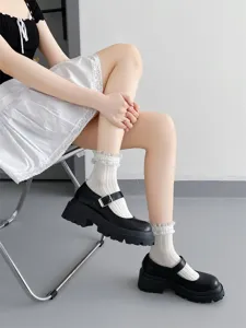 Detailed shot of white ruffled lace socks paired with black platform Mary Jane shoes on model.