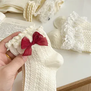 Detail shot of white Lolita socks featuring delicate lace ruffles and a dark red sheer bow.