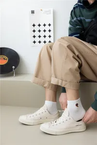 Primo piano dettagliato di calzini bianchi in cotone con lettera R ricamata, indossati con scarpe.