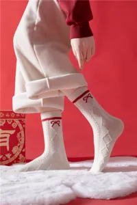 Vue détaillée de chaussettes festives pour femmes en tricot avec nœud rouge et motif losange.