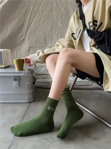 Close up of green ribbed crew socks with outdoor embroidery, camping style lifestyle detail shot.