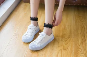 Detailed shot of women's black lace ruffle ankle socks paired with casual white canvas shoes.