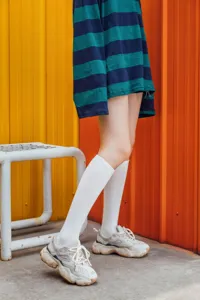Detailansicht stilvoller weißer Wadensocken kombiniert mit klobigen Sneakers und gestreiftem Top.