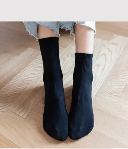 Detail shot of classic black crew socks worn on wooden background, showing fine ribbed texture.