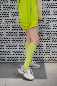 Nahaufnahme von leuchtend neongrünen Wadensocken kombiniert mit Chunky Sneakern vor Strukturwand.
