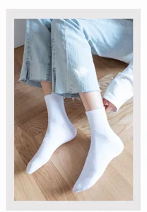 Detail view of classic white mid-tube cotton socks worn by model on wooden floor.