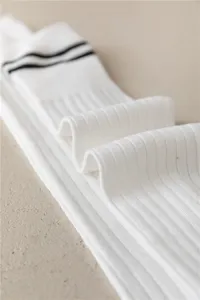 Nahaufnahme von weißen Sport-Knie-Socken mit schwarzen Streifen und Rippstrick-Details.