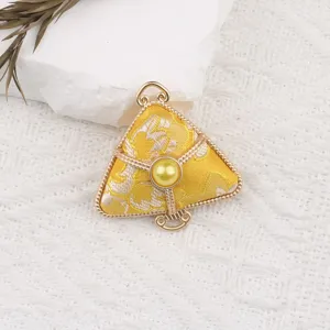 Close-up detail view of traditional yellow brocade zongzi pendant with metal frame.