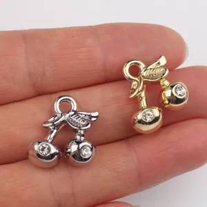 Close-up of double cherry charms in gold and silver alloy with sparkling zircon for DIY jewelry.