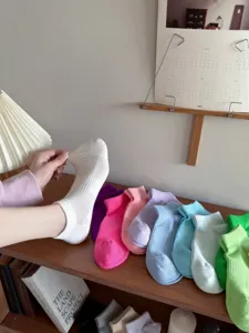 Detailansicht atmungsaktiver Mesh-Kurzsocken in Bonbonfarben auf Holzregal Hintergrund präsentiert.