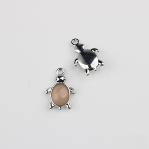 Detailed shot of two cute turtle metal charm pendants with pink cabochon and silver back.