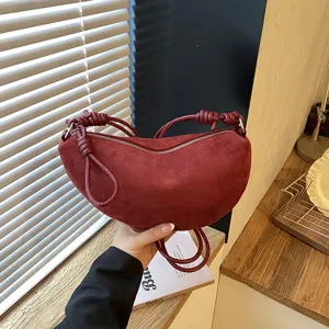 Gros-plan du sac croissant en daim rouge vin avec des details de noeuds elegants.