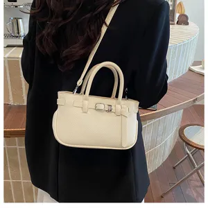 Gedetailleerde opname van een chique crèmekleurige mini-handtas met gesp en schouderriem.
