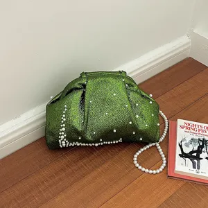 Detailed close-up view of the dark green shiny pearl shell evening bag on wood floor.