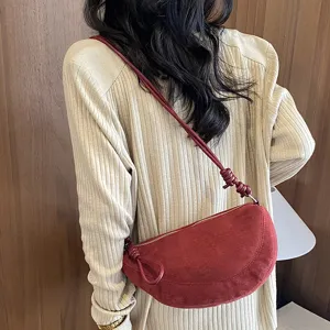 Vue detaillee d un sac bandouliere croissant en sude rouge fonce avec laniere noeud.
