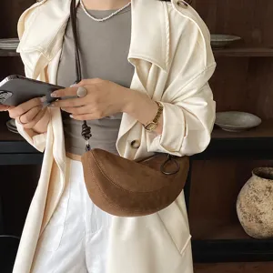 Gros plan sur le sac croissant en daim marron élégamment assorti au trench-coat.