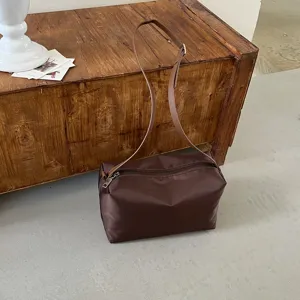 Dettaglio borsa a spalla in nylon marrone con sottile tracolla su una vecchia cassa in legno rustica.