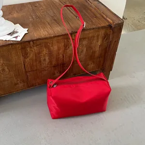 Scatto dettagliato della borsa a spalla rossa minimalista, che evidenzia la sua texture e zip.