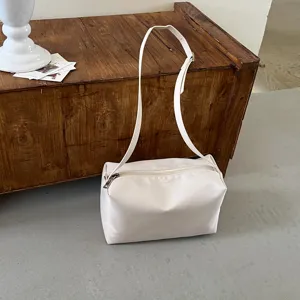 Dettaglio della borsa a spalla minimalista color avorio con cerniera liscia e cinturino.