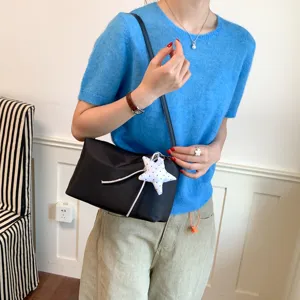 Dettaglio borsa a spalla nera minimalista, con tracolla sottile e ciondolo a forma di stella.
