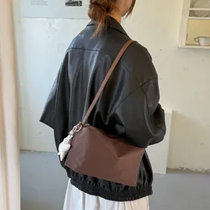 Dettaglio della borsa a spalla marrone minimalista indossata dal modello, stile leggero.