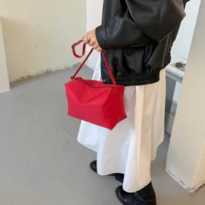 Dettaglio borsa a spalla rossa in nylon con forma a cuscino minimalista e chiusura a zip.