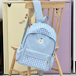 Détail de sac à dos scolaire à carreaux bleu clair, avec broderie de pomme et poche avant.