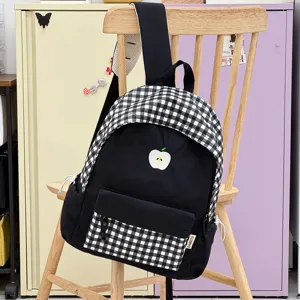 Détail rapproché du sac à dos scolaire à carreaux noir et blanc avec une broderie de pomme.