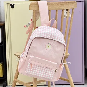 Gros plan détaillé d'un sac à dos d'écolier à carreaux roses avec broderie de pomme sur une chaise.