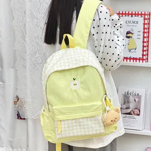 Détail du sac à dos à carreaux jaunes avec broderie pomme et pendentif ours pour voyage.