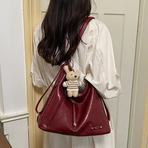 Detail view of wine red PU leather slouchy shoulder bag with cute bear pendant and metal tag.