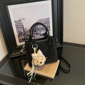 Primer plano detallado del elegante bolso saco negro con un lindo dije de osito de peluche.