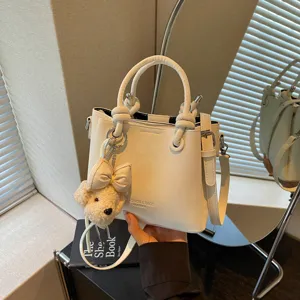 Vista detallada de un bolso cubo blanco de moda con bonito llavero de peluche y correa ajustable.