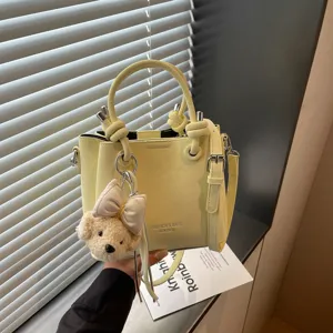 Detalle de bolso cubo de cuero amarillo con asa, herrajes y lindo llavero de osito de peluche.
