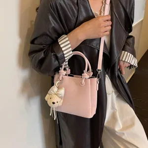 Bolso bandolera tipo bombonera de cuero rosa para mujer con lindo dije de oso y asas.