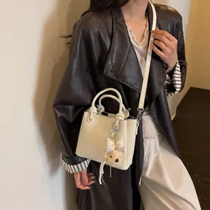 Detalle del bolso tipo cubo blanco de estilo coreano con cuero suave y osito colgante.