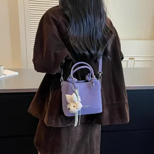 Vista detallada del bolso tipo cubo morado con bonito colgante de peluche y correa.