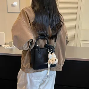 Elegante bolso bombonera de cuero negro para mujer con correa de hombro y bonito colgante de peluche.