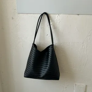 Detail view of a black woven leather tote bag hanging on a rustic vintage textured wall.