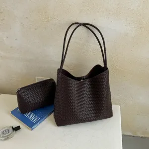 Detailed view of dark brown woven leather tote bag and matching pouch on minimal table.