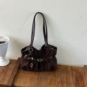 Vista dettagliata di una elegante borsa a spalla marrone morbida con ciondolo e fibbia chic.
