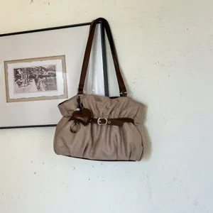 Vista dettagliata della chic borsa a spalla kaki arricciata con cinturini marroni e ciondolo.