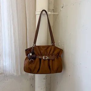 Dettaglio borsa a spalla arricciata marrone, design chic minimalista con ciondolo a cuore e cintura.