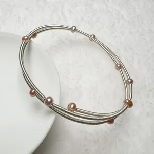 Detail view of multi-layer silver wire bracelet adorned with pink pearls on white plate.