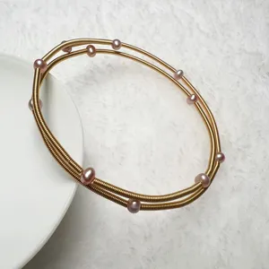 Details of multi-layer gold coiled wire bracelet with pink freshwater pearls, elegant design.
