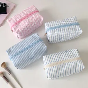 Detailed view of fresh pastel striped and checkered cosmetic bags with cute bow embroidery.