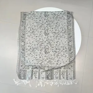 Close-up detail of a grey ethnic paisley jacquard shawl featuring elegant white tassels