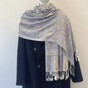Detailed view of ethnic paisley jacquard shawl with white tassels on black coat.
